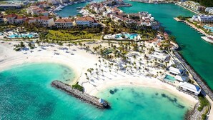 Vista aérea de un complejo turístico costero con varios edificios, un puerto deportivo y una playa.