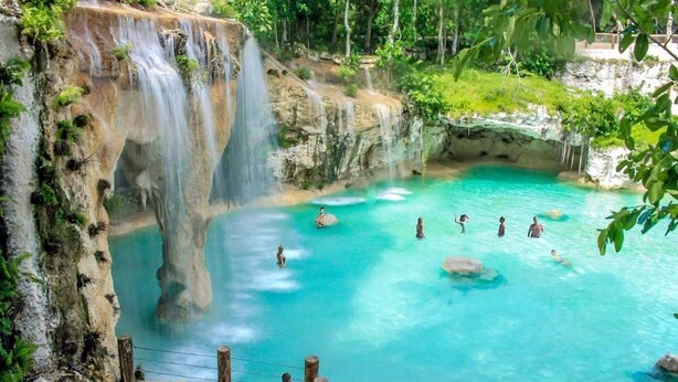Una piscina natural con agua turquesa cristalina, rodeada de acantilados rocosos y abundante vegetación.