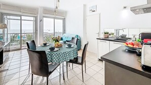 Ein Essbereich mit Tisch für zwei, eine Küche mit Obstschale und ein Balkon mit Blick.