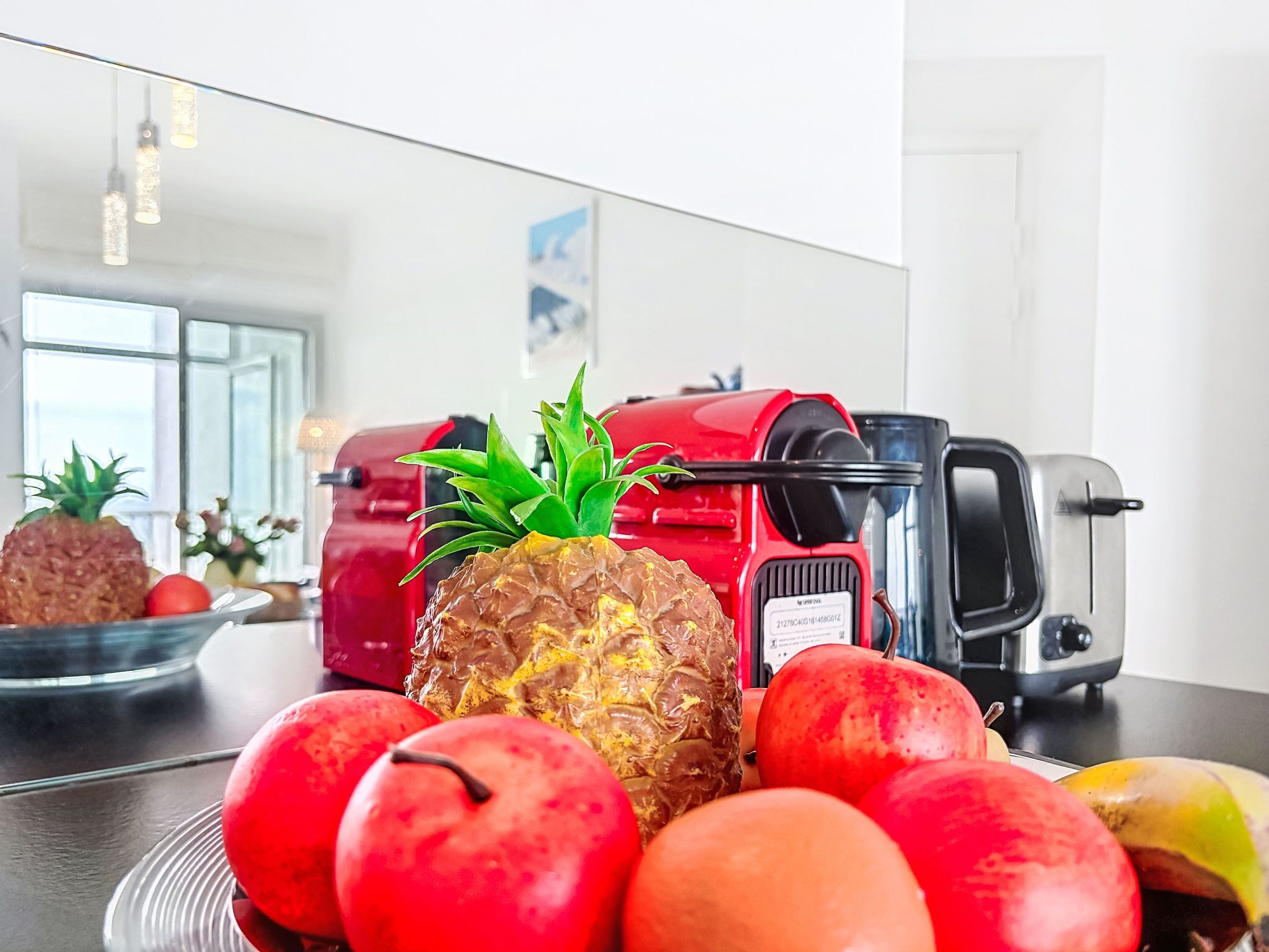 Un comptoir de cuisine avec un appareil rouge, un grille-pain et divers fruits, notamment des pommes et un ananas.
