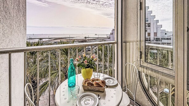 Ein Balkon mit Tisch für zwei Personen, mit Blick auf Strand und Stadtlandschaft.