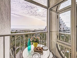 Un balcón con una mesa para dos, con vista a la playa y al paisaje urbano.