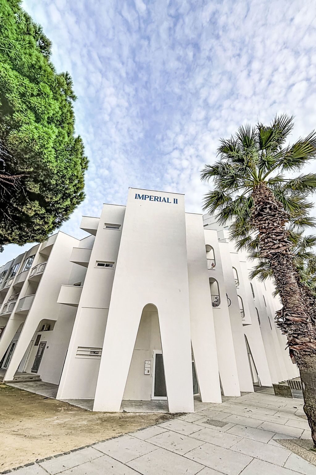 Un bâtiment moderne, surmonté d’une enseigne indiquant « IMPERIAL II », qui se distingue par son architecture originale, avec de nombreux balcons et des ouvertures en arc de cercle.
