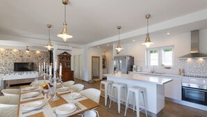 Una cocina moderna con una isla central, taburetes blancos y luces colgantes.
