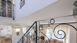 Amplia sala de estar con escalera, un conjunto de sofás y un comedor con cocina al fondo.
