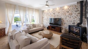 Una sala de estar con una pared de piedra, un televisor de pantalla plana, un sofá, un banco de madera y una chimenea.