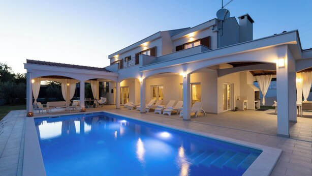 Una casa moderna de dos pisos con piscina, mobiliario exterior y un patio cubierto.