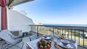 A balcony with a table set for dining, a chair, a basket of fruit, and a view of the sea. - Les Grenadines by Interhome (La Grande Motte)