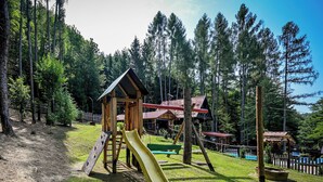 Une aire de jeux avec un toboggan, des structures d’escalade et un petit bâtiment.