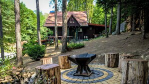 Une cabane rustique dotée d’un espace de détente circulaire, entourée d’arbres et bordée d’un chemin pavé.