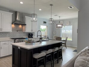 A modern kitchen with white cabinets, a central island with bar stools, pendant lighting, and a view to the outdoors. - Charming house in the heart of Mission with Pool (Mission)