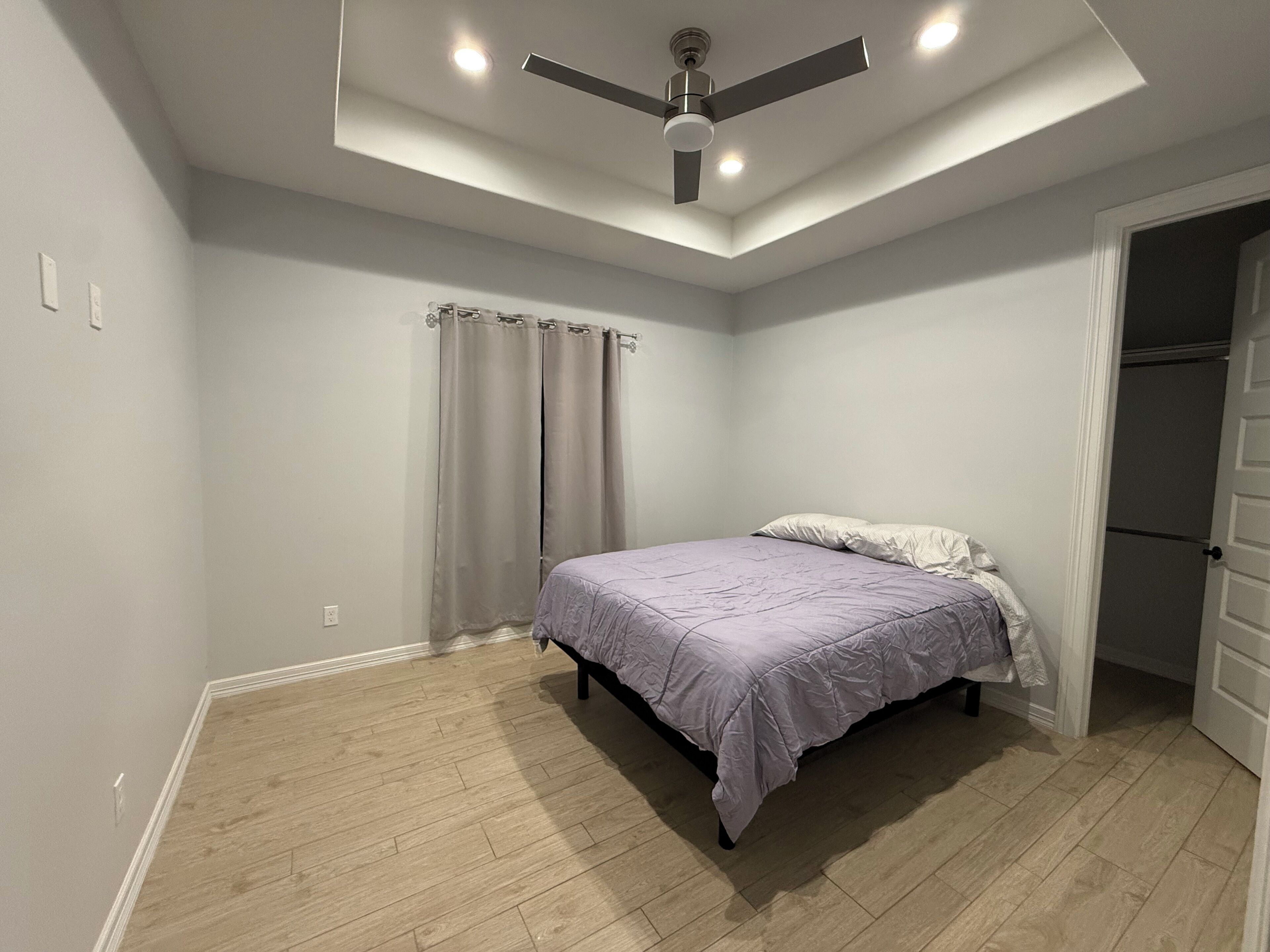 A bedroom with a bed, a ceiling fan, a door, and a light switch.