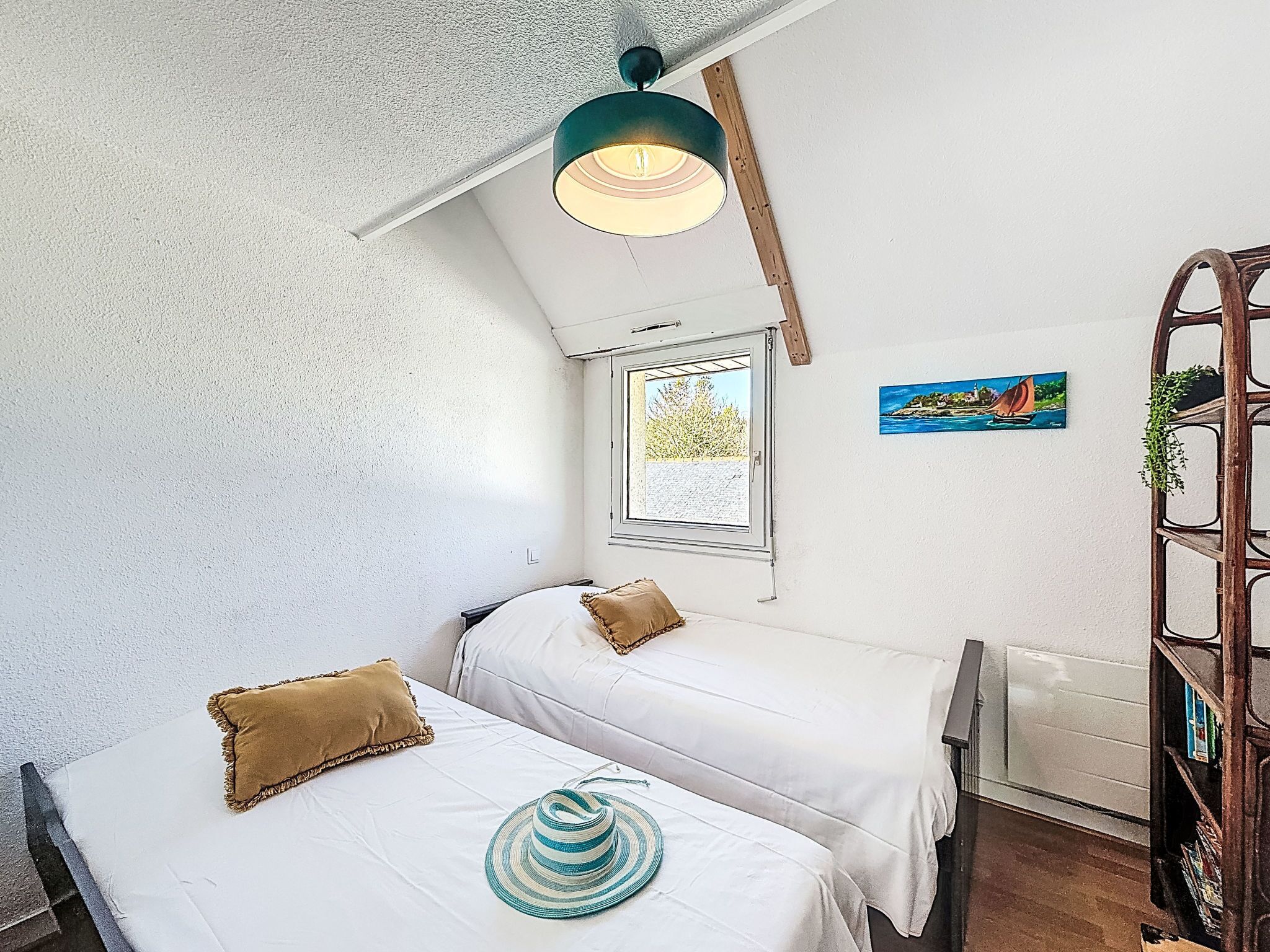 Une chambre avec deux lits, une fenêtre, un tableau et une échelle en bois.