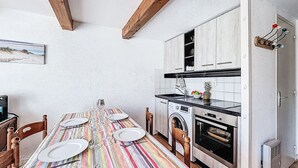 A dining table set with plates and wine glasses, a kitchen with a washing machine, and a wooden ceiling. - Les Jardins de la Plage by Interhome (Carnac)