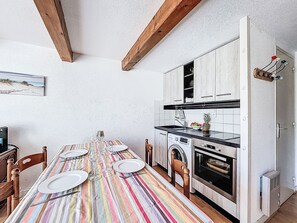 Ein Esszimmer mit gedecktem Tisch, Geschirr und Weingläsern, eine Küche mit Waschmaschine und eine Holzbalkendecke.