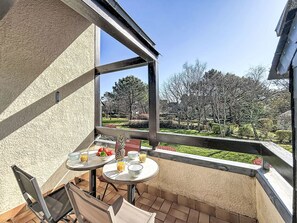 A balcony with a table set for two, a chair, and a view of a landscaped garden. - Les Jardins de la Plage by Interhome (Carnac)