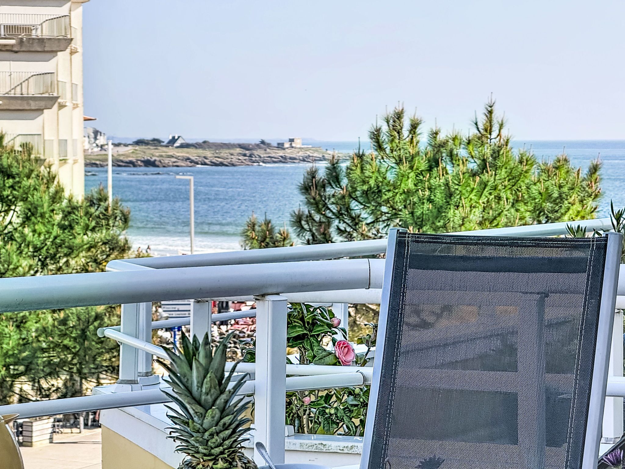 Uma varanda com vista para o oceano, uma cadeira e algumas plantas.
