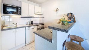 A compact kitchen with a microwave, sink, and a small countertop with stools. - Le Hoche by Interhome (Quiberon)