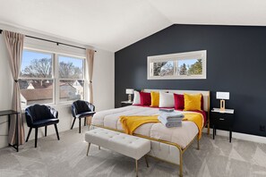 A bedroom with a bed, two chairs, a bench, a nightstand, and a window.