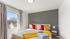Un dormitorio con cama, mesita de noche, ventana con cortinas y pared con diseño.
