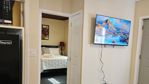 A living room with a flat-screen TV mounted on the wall, a refrigerator, and a sofa. - Enjoy a piece of home in a cozy inviting space. (Waynesboro)