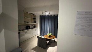 Cocina compacta con microondas, cafetera y una pequeña mesa de comedor con una planta.