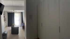 Una habitación con una cama, una mesita con una planta, una ventana con cortinas y una puerta.