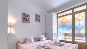 A bedroom with a bed, pillows, a lamp, a window with geometric glass, and two wall art pieces. - Milanković by Interhome (Vrsar)