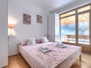 A bedroom with a bed, pillows, a lamp, a window with geometric glass, and two wall art pieces. - Milanković by Interhome (Vrsar)