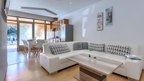 A modern living room with a white sofa, wooden coffee table, and a kitchen in the background. - Milanković by Interhome (Vrsar)