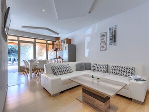 A modern living room with a white sofa, wooden coffee table, and a kitchen in the background. - Milanković by Interhome (Vrsar)