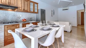 A modern kitchen with granite countertops, wooden cabinets, and a dining area with white chairs and a white table set for four. - Milanković by Interhome (Vrsar)