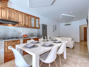 A modern kitchen with granite countertops, wooden cabinets, and a dining area with white chairs and a white table set for four. - Milanković by Interhome (Vrsar)
