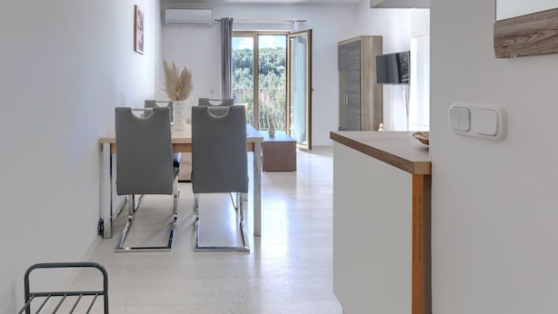 A modern kitchen with a built-in oven, a dining area with a table and chairs, and a large window with a view of greenery. - Milanković by Interhome (Vrsar)