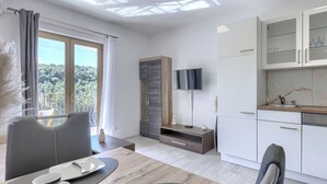 A modern kitchen with a built-in TV, a dining area with a table set for two, and a balcony with a view of the greenery. - Milanković by Interhome (Vrsar)