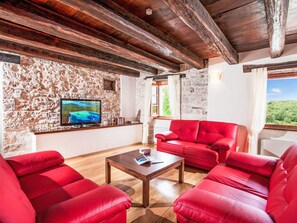 A room with stone walls, a wooden ceiling, a red sofa, a coffee table, and a TV on the wall. - Poropati by Interhome (Grožnjan)