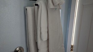 A bathroom with a towel rack holding several towels, a door with a handle, and a towel bar.
