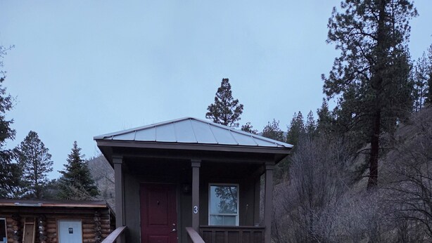 A wooden cabin with a red door, a small porch, and a metal ramp leading to the entrance.