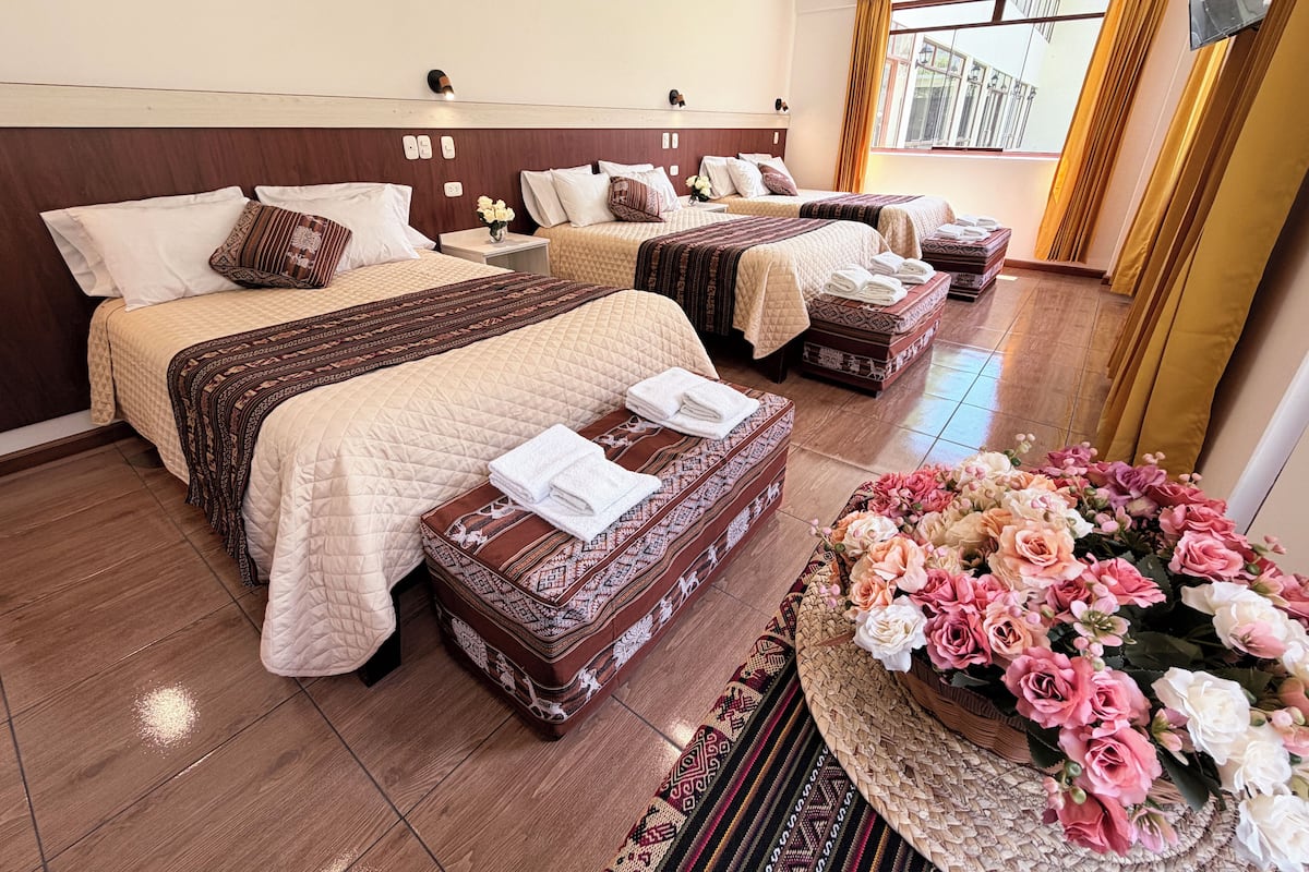 A hotel room with three beds, a large window, and a decorative floral arrangement.