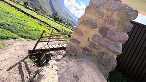 A stone structure with a wooden bridge, a mountainous backdrop, and a building with a sloped roof. - Boutique Inka Hotel (Ollantaytambo)