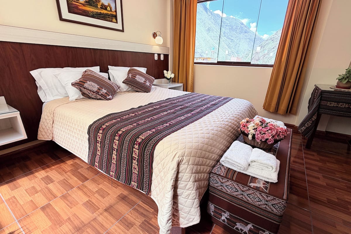 A hotel room with a bed, a nightstand, a window with curtains, a framed picture on the wall, and a wooden floor.