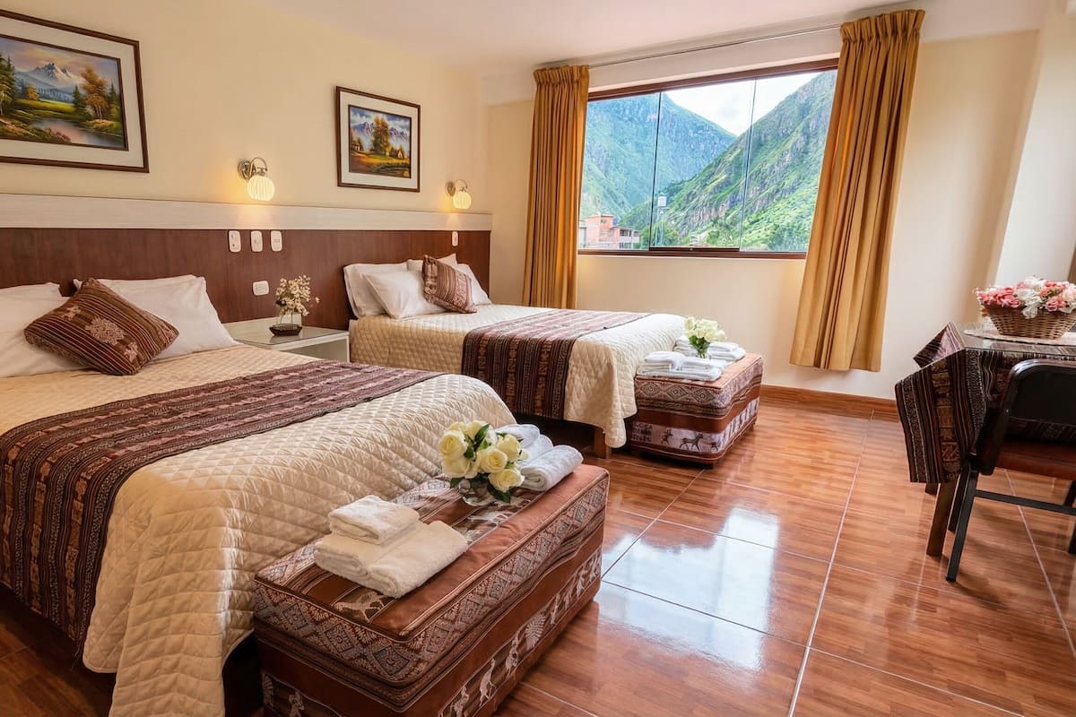 A hotel room with two beds, a wooden headboard, a large window with a mountain view, and a small table with flowers.