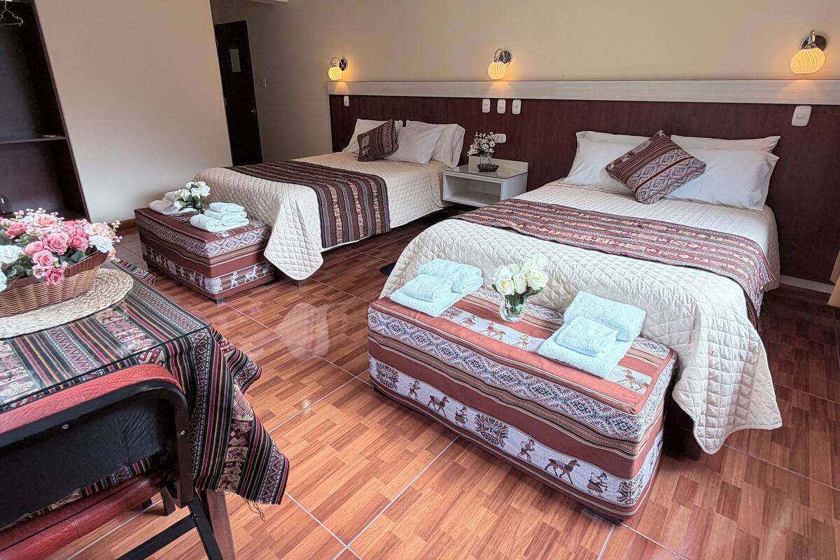 A hotel room with two beds, a sitting area with a chair, a small table with a vase of flowers, and a nightstand with a lamp.