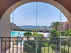 A balcony with a view of a swimming pool, palm trees, and a marina. - Les Rivages de Coudoulière by Interhome (Six Fours La Coudoulière)