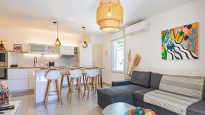 Eine moderne Küche mit weißen Schränken, einem Essbereich mit Barhocker, einem grauen Sofa und einem farbenfrohen abstrakten Gemälde an der Wand.
