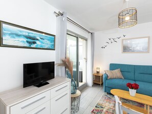A modern living room with a flat-screen TV, a blue sofa, a coffee table with red flowers, and a colorful rug. - L'Albatros by Interhome (Dinard)