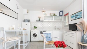A modern kitchen with a washing machine, oven, and dining area with a table and chairs. - L'Albatros by Interhome (Dinard)