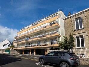 Um edifício residencial com vários andares, varandas, garagem e acesso por portão fechado.