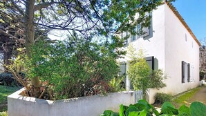 Ein weißes Gebäude mit Garten, einem Betonpflanzgefäß und einem Baum.