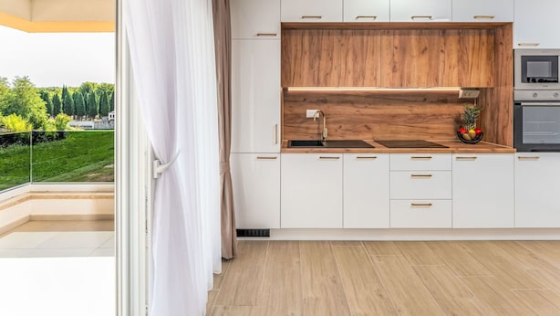 A modern kitchen with white cabinets, a wooden accent wall, a built-in oven, and a view of a green landscape. - Mediterranee Oliva by Interhome (Poreč/Funtana)